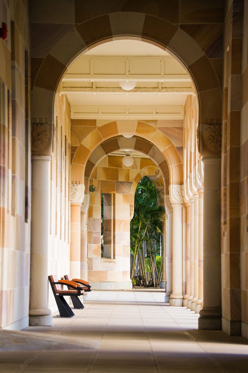 A sandstone cloister corridor with columns and long shadows, in ink duotone.
