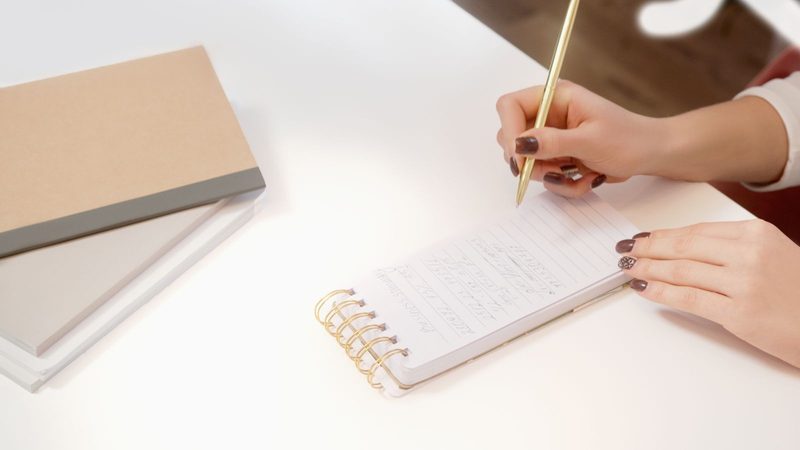 A hand writing in a notebook beside a closed book, in ink duotone.