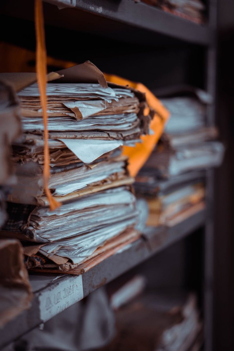 Bundles of paper files stacked on a shelf, in ink duotone.